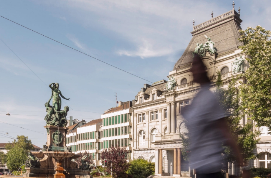 Innenstadt Häuserfasade, im Vordergrund unscharfe Person und Brunnen mit Statue