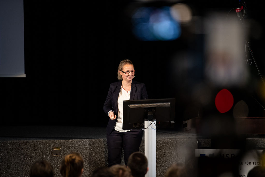 Susanne Schmidt-Rauch steht schmunzelnd auf der Bühne hält einen Vortrag.