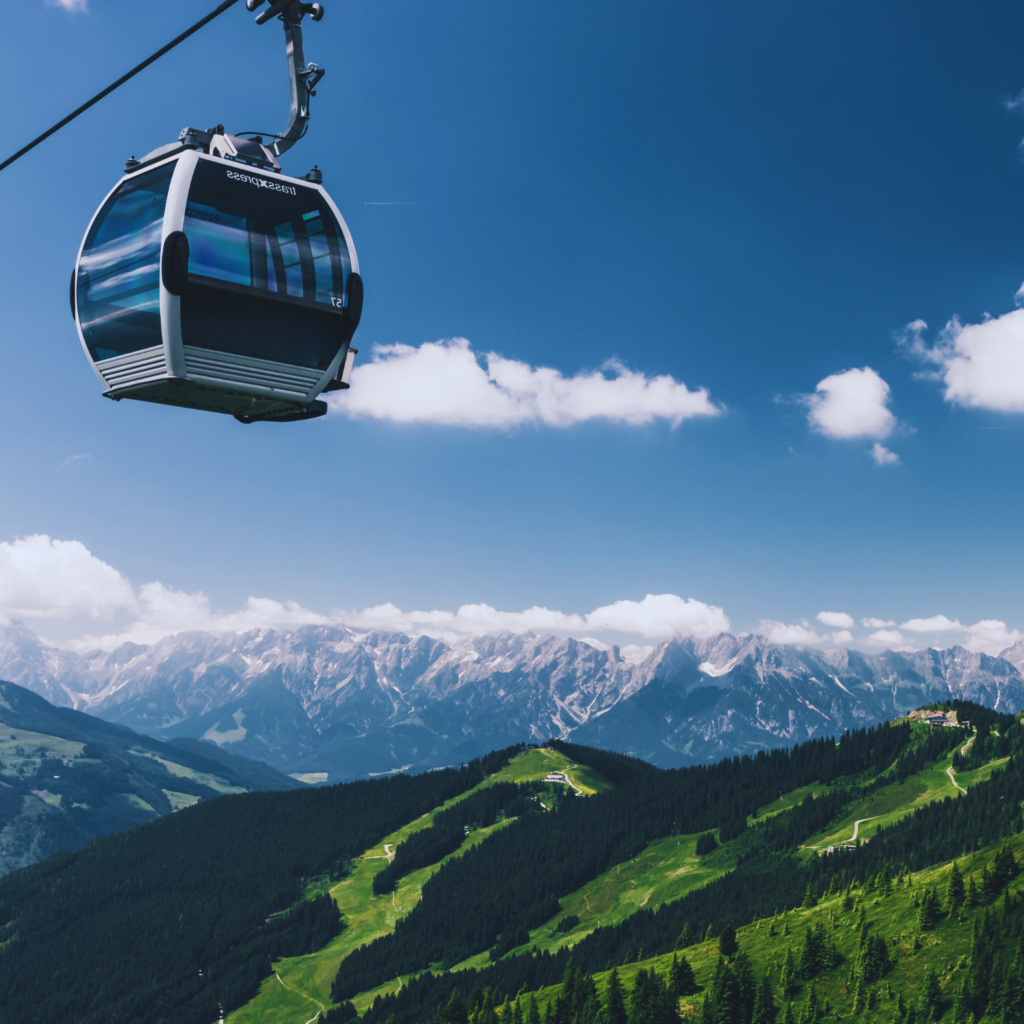 Gondel einer Bergbahn in der Luft mit einem Panorama aus schneebedeckten und näher liegenden, grün bewachsenen Bergen. Symbolbild für Customer Experience im alpinen Tourismus.